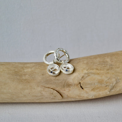 Silver button earrings on a piece of driftwood with a gray background