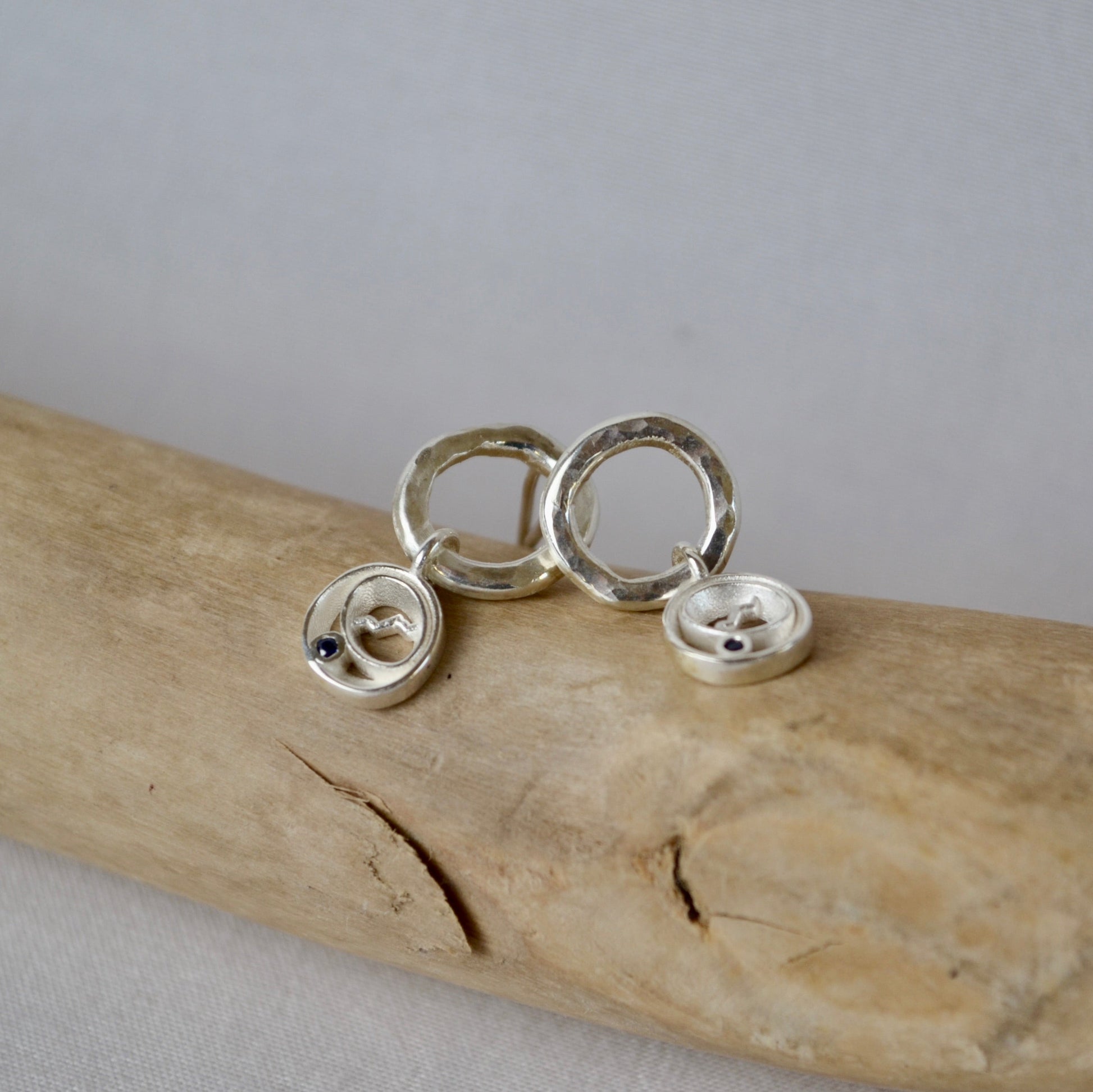 Silver earrings on a piece of driftwood with a plain background