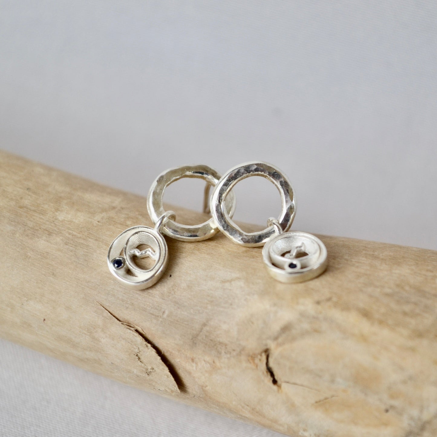 Silver circular earrings on a piece of driftwood with a gray background