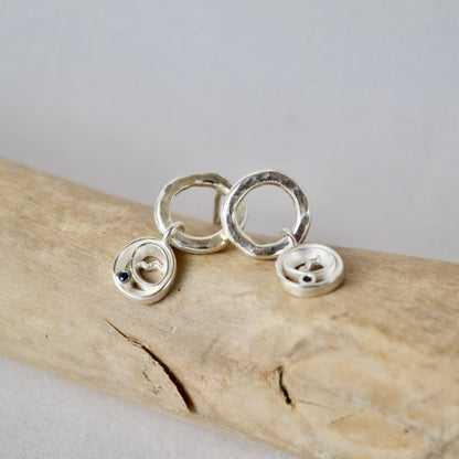 Silver circular earrings on a piece of driftwood with a gray background