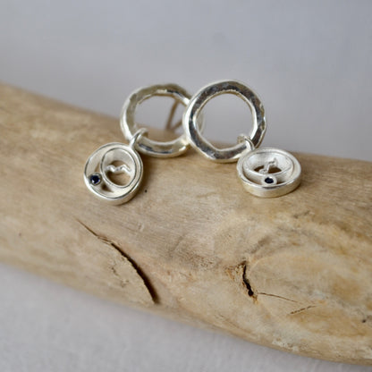 Silver earrings on a piece of driftwood with a neutral background