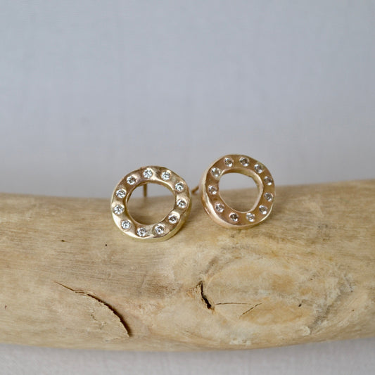 Gold hoop earrings with small diamonds on a piece of driftwood against a light gray background