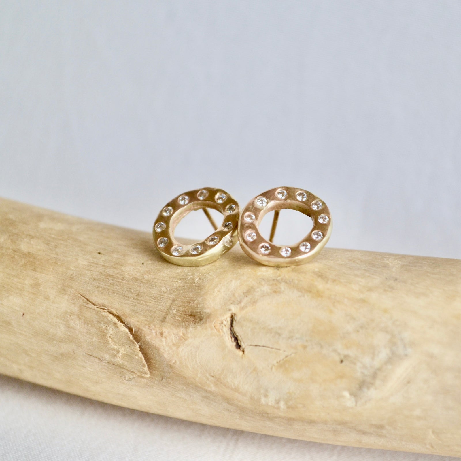 Gold stud earrings with clear stones on a piece of driftwood against a light background