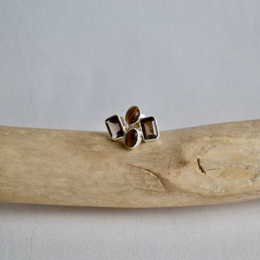 Silver ring with embedded stones on a piece of driftwood against a gray background