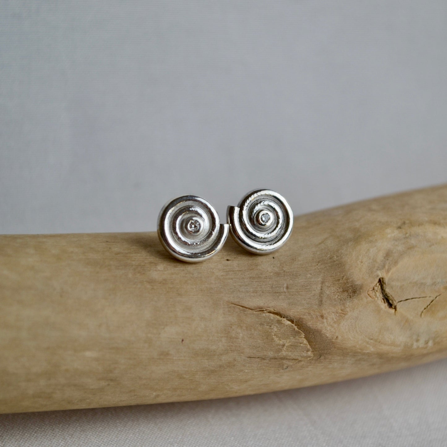Silver spiral earrings on a piece of driftwood with a gray background