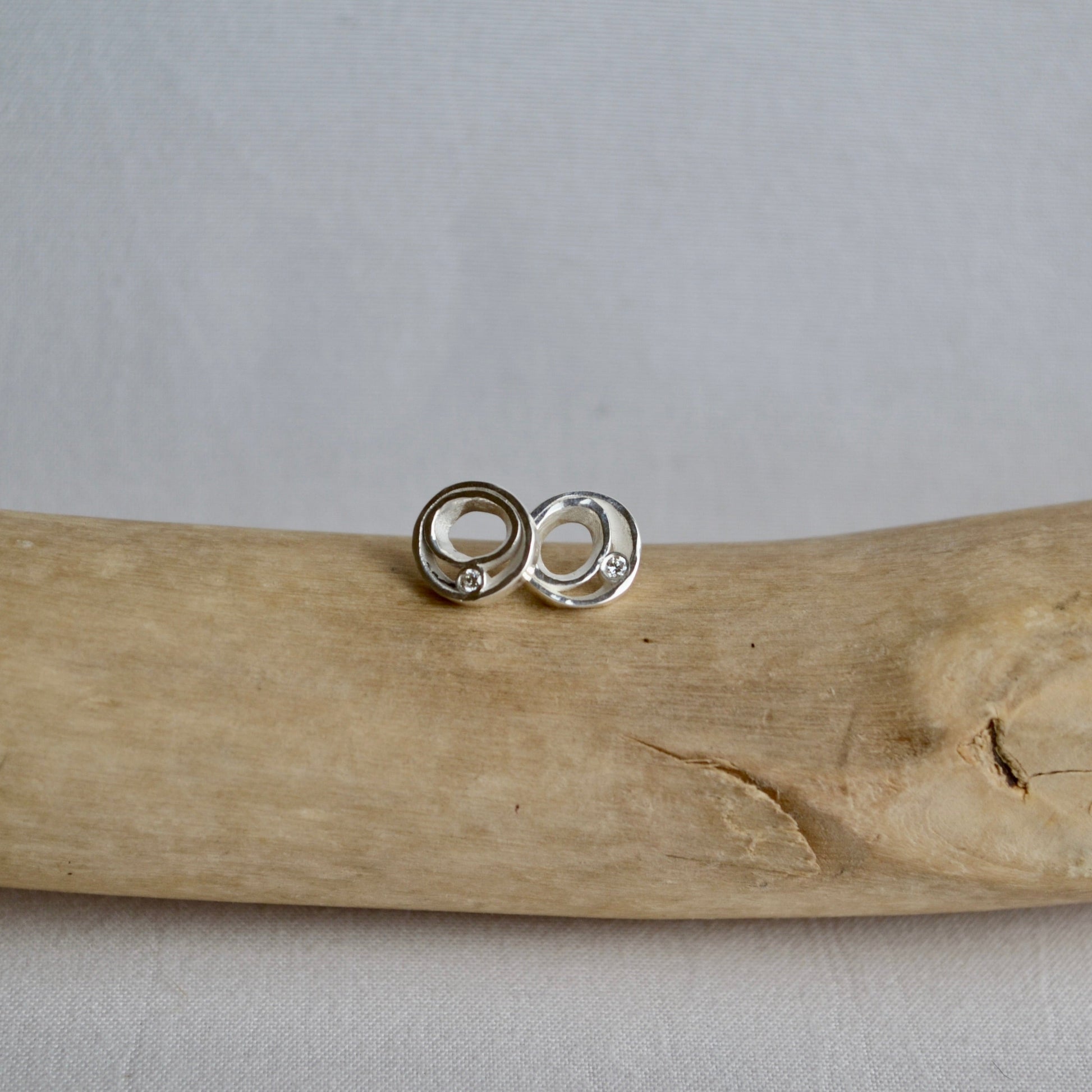 Silver earrings on a piece of driftwood with a neutral background