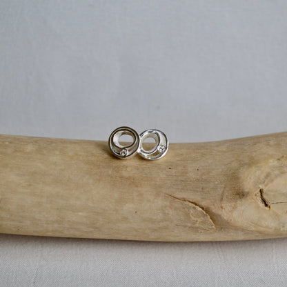 Silver earrings on a piece of driftwood with a neutral background