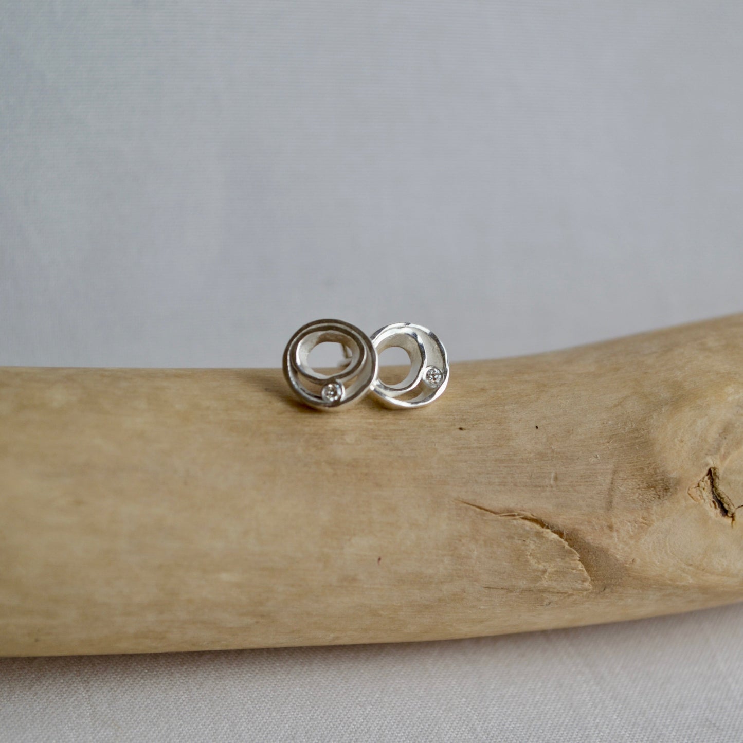 Silver earrings on a piece of driftwood with a gray background