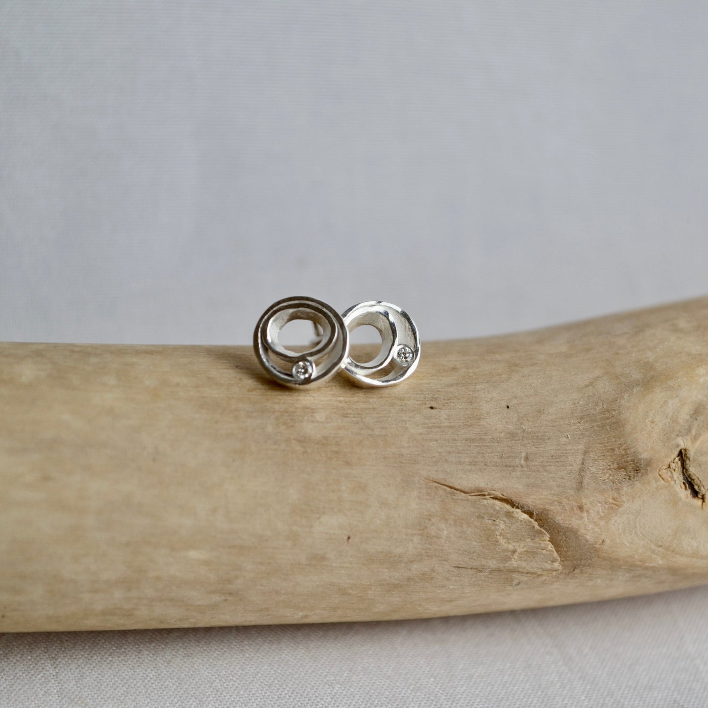 Silver earrings on a piece of driftwood with a gray background