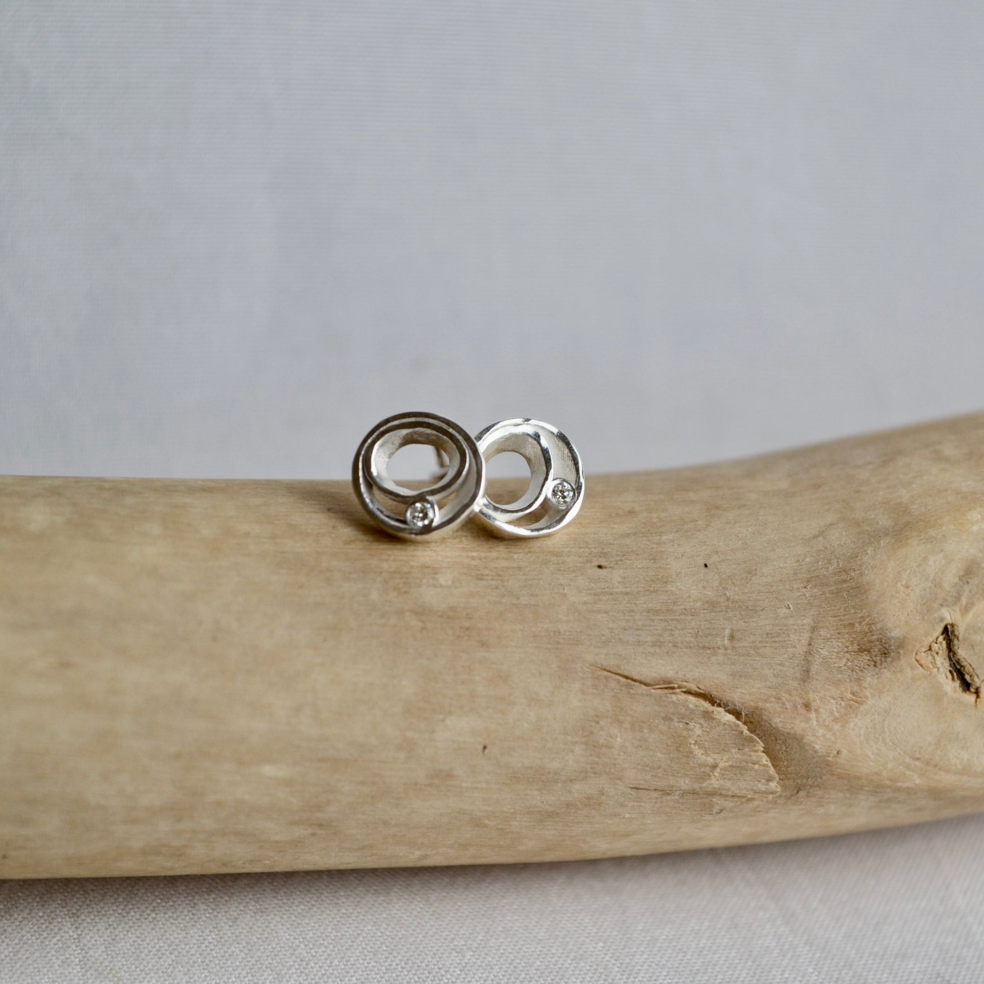Silver earrings on a piece of driftwood with a gray background