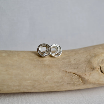 Silver earrings on a piece of driftwood with a gray background