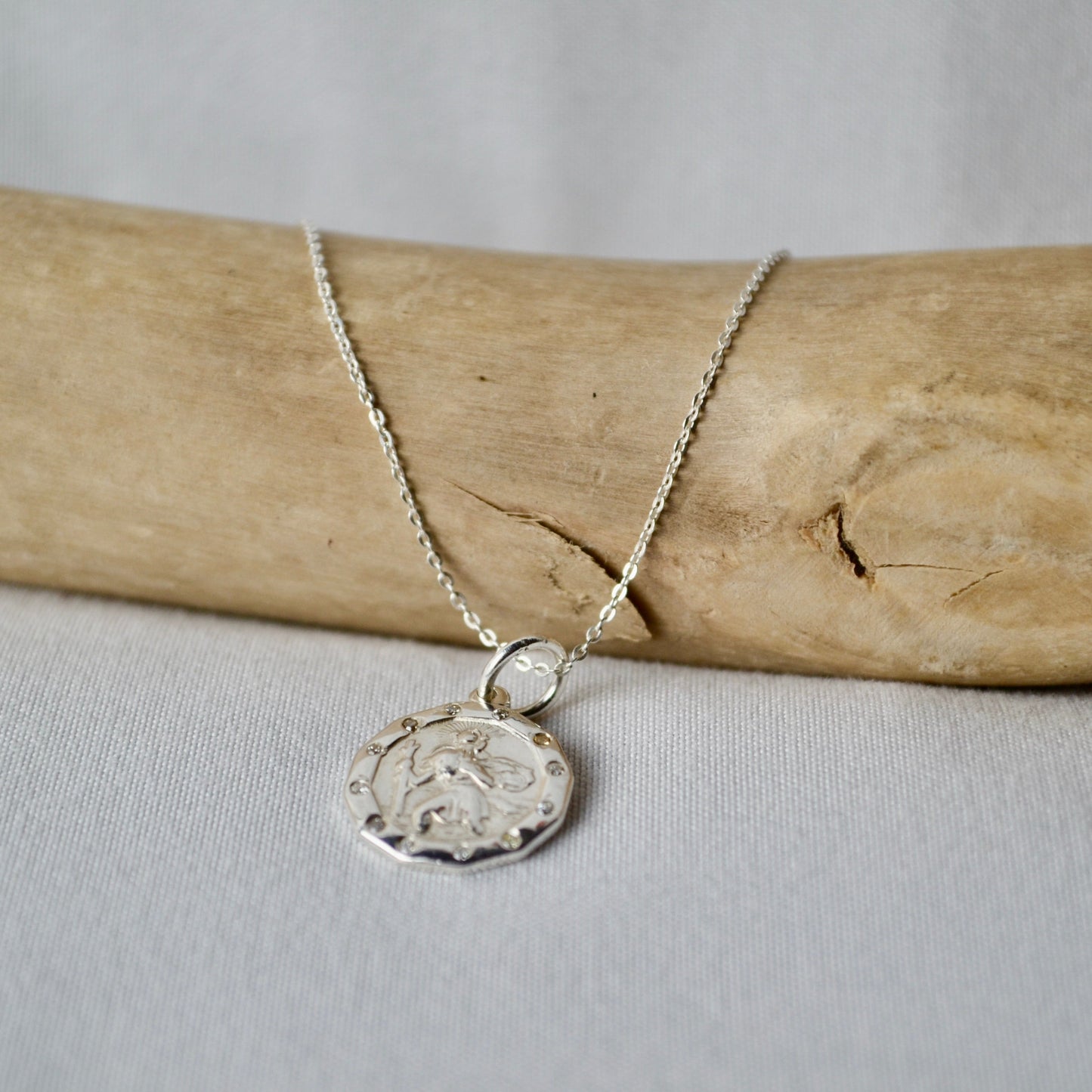 Silver necklace with a pendant on a piece of driftwood against a light background