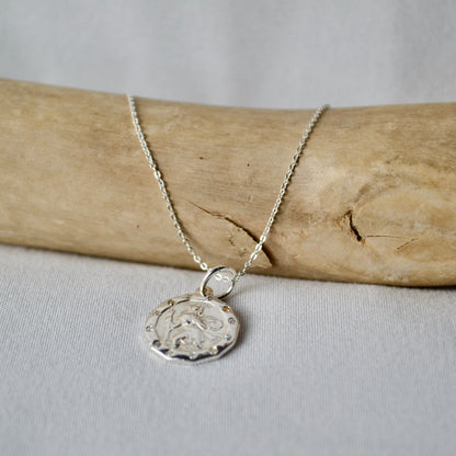 Silver necklace with a pendant on a piece of driftwood against a light background