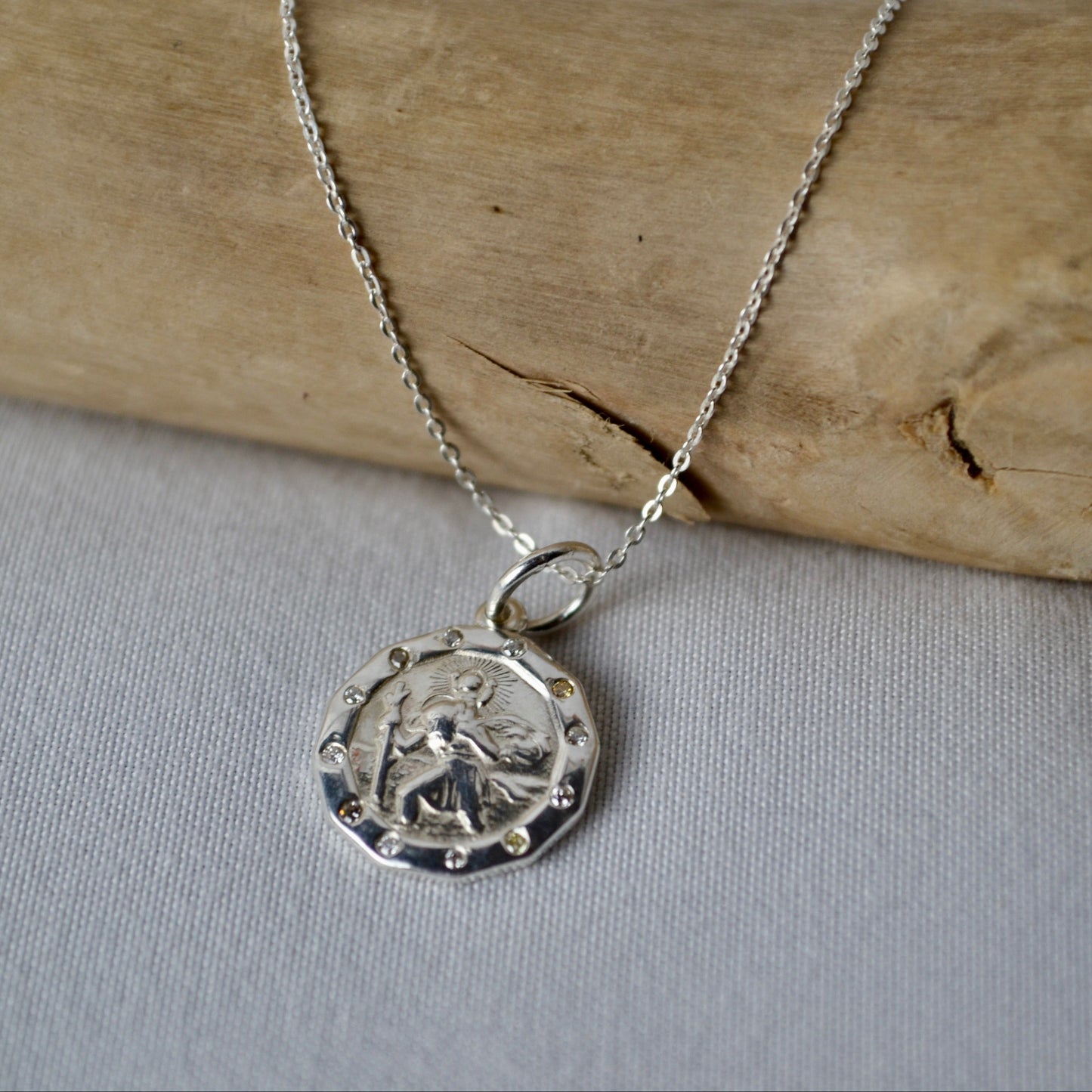 Silver necklace with a pendant on a wooden stick and light fabric background