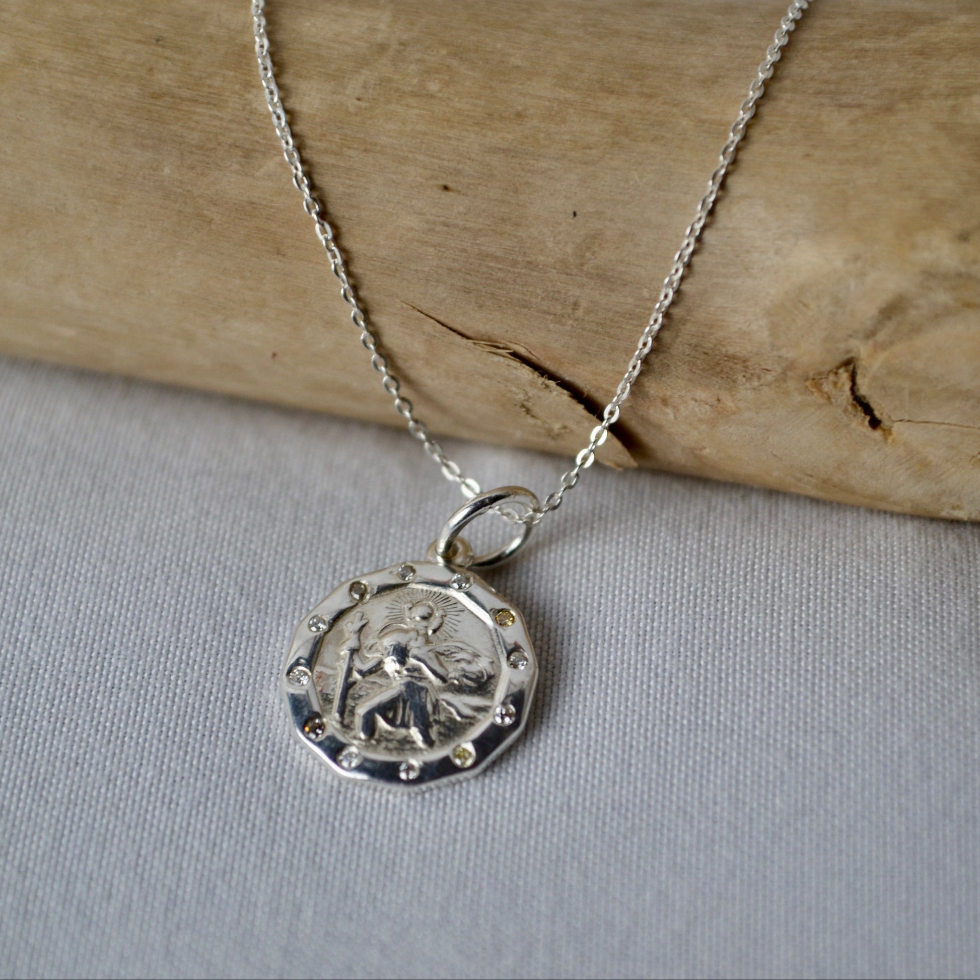 Silver necklace with a pendant on a wooden stick and light fabric background