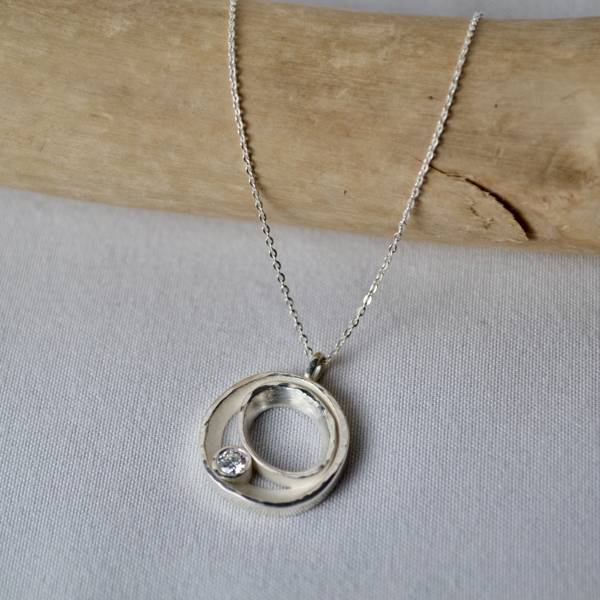 Silver necklace with a circular pendant on a light gray background