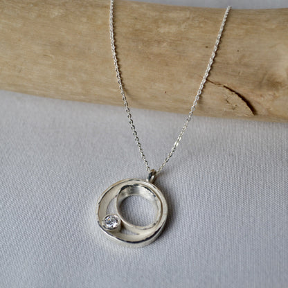Silver necklace with a circular pendant on a light gray background
