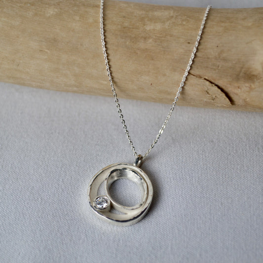 Silver necklace with a circular pendant on a light gray background