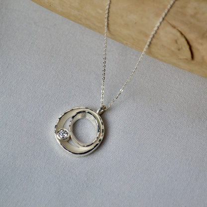 Silver necklace with a circular pendant on a light gray fabric background