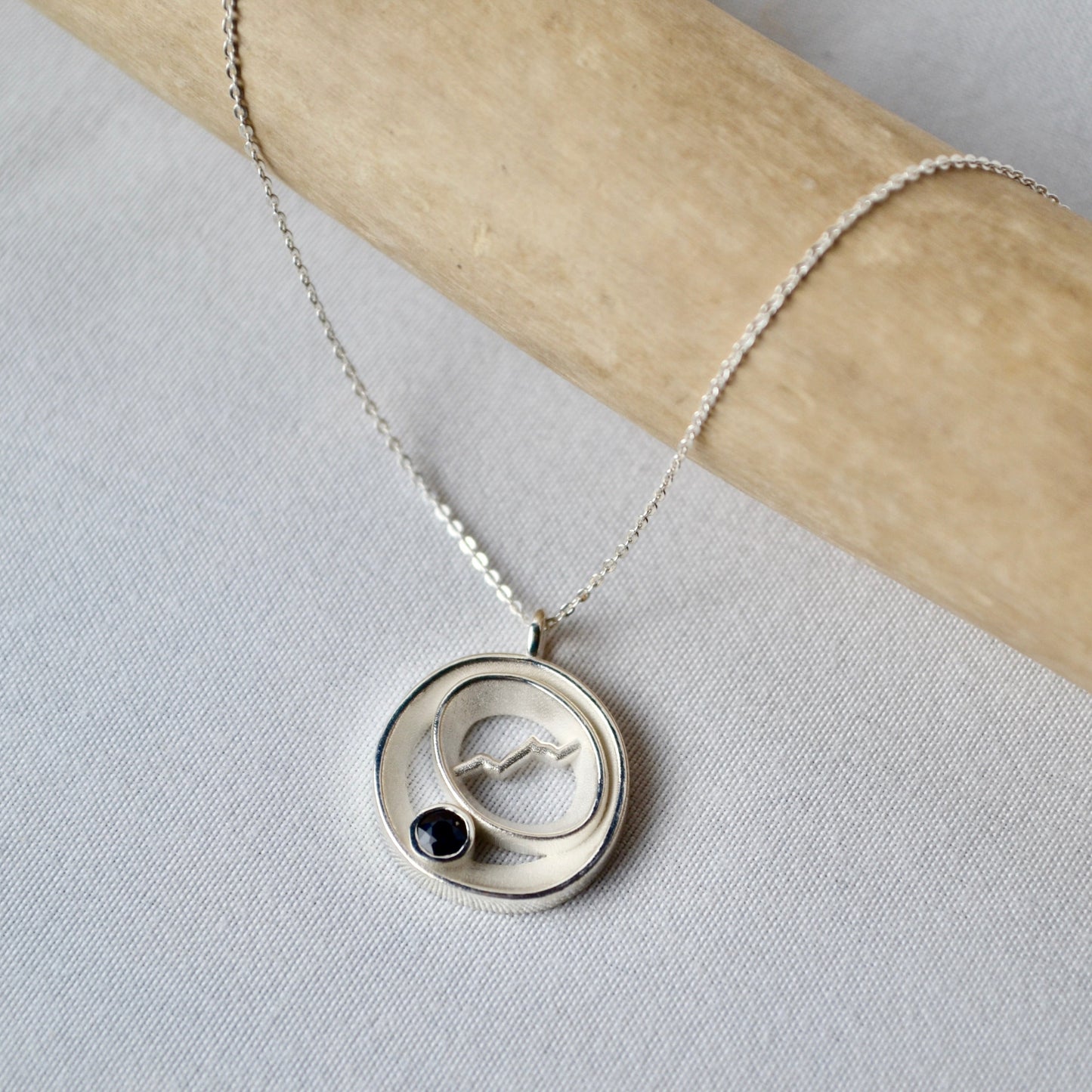 Silver necklace with a circular pendant featuring a black stone on a light gray background