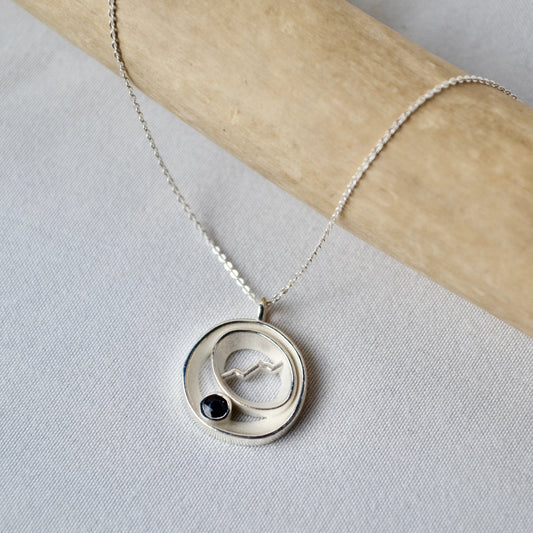 Silver necklace with a circular pendant featuring a black stone on a light gray background