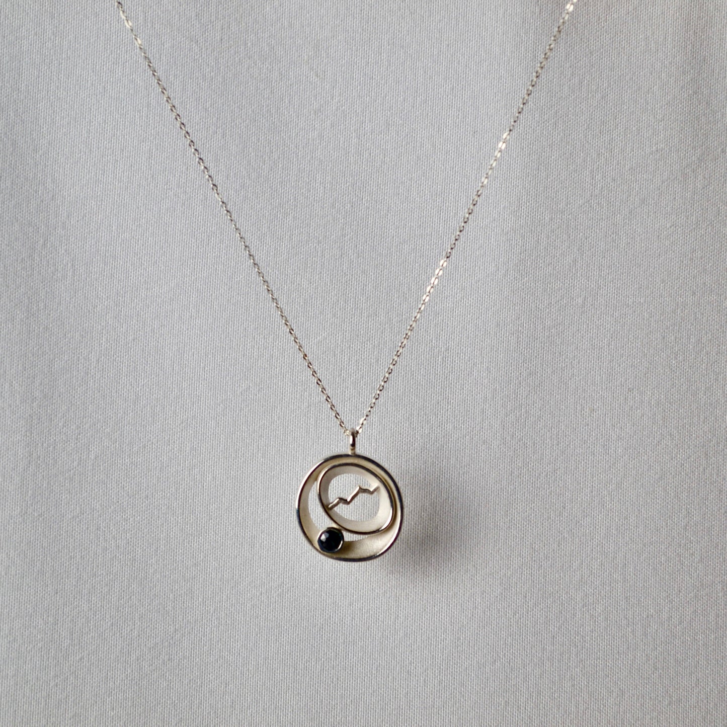 Silver necklace with a circular pendant on a light gray background