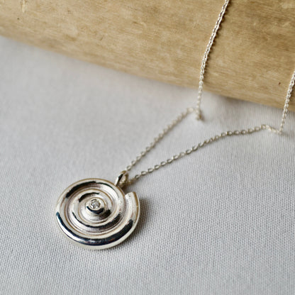 Silver necklace with a circular pendant on a light gray surface