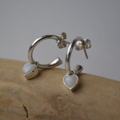 Silver hoop earrings with heart-shaped gemstones on a wooden surface