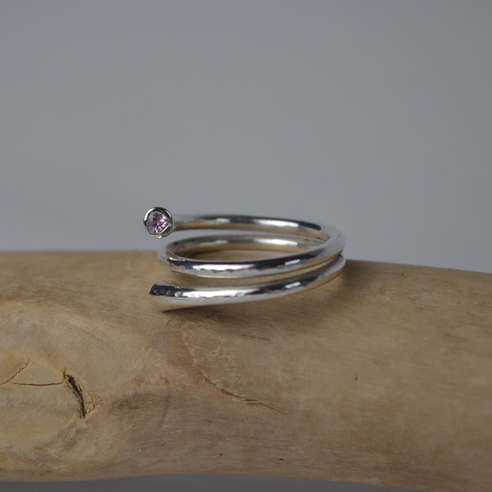 Silver ring with a pink gemstone on a wooden surface