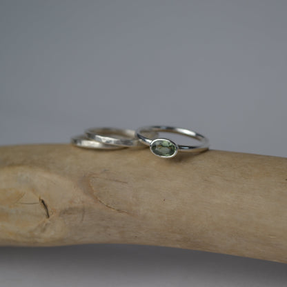 Two silver rings with green gemstones on a wooden surface