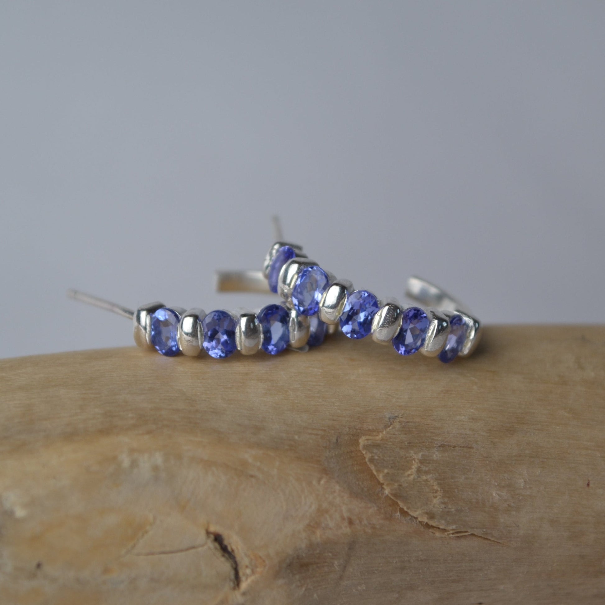 Silver hoop earrings with purple gemstones on a wooden surface