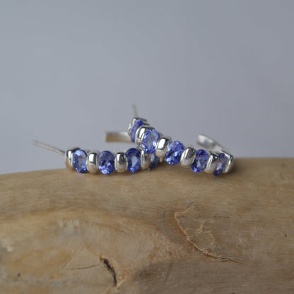 Silver hoop earrings with purple gemstones on a wooden surface