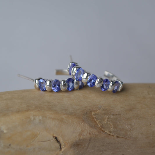 Silver hoop earrings with purple gemstones on a wooden surface