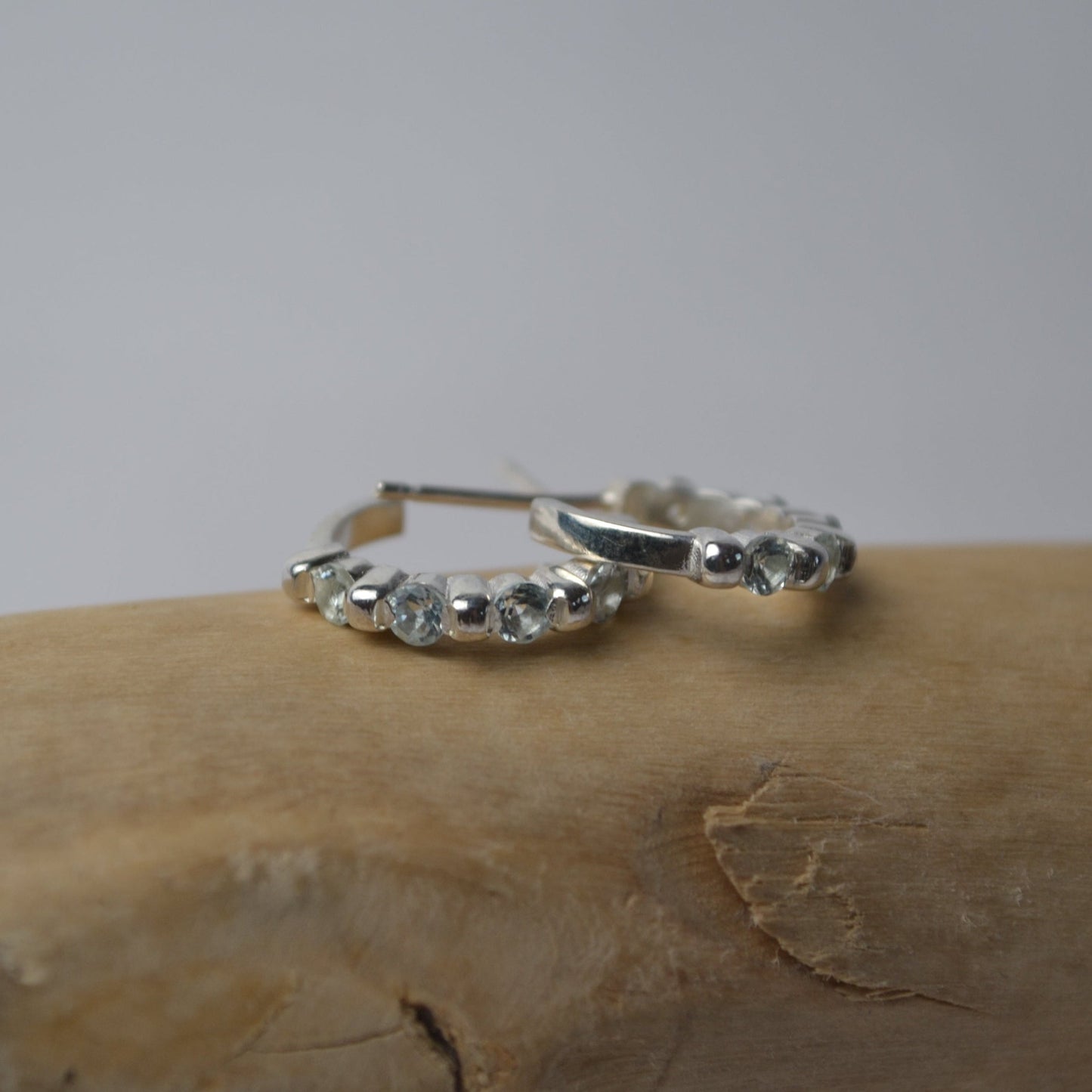 Silver hoop earrings with small stones on a wooden surface