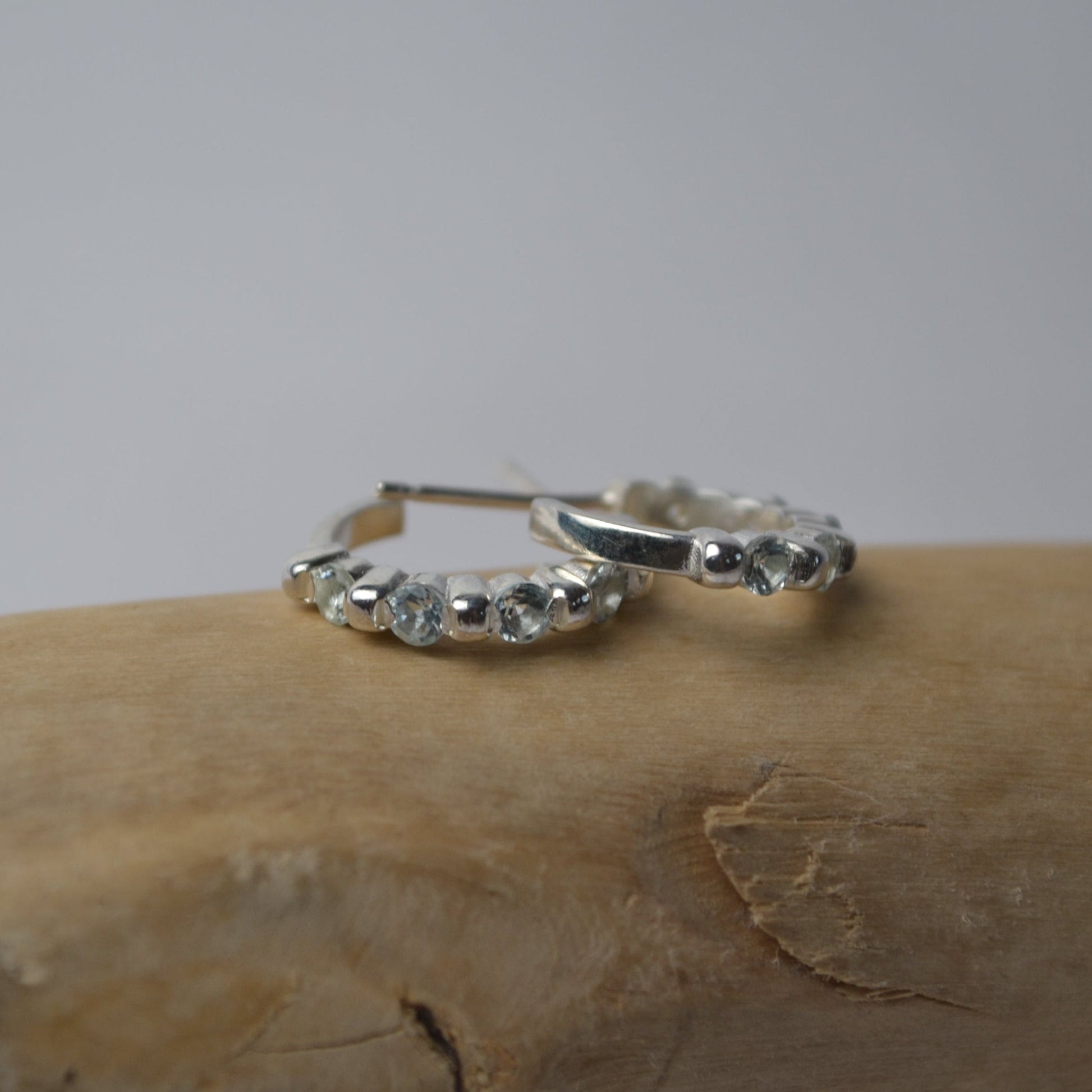 Silver hoop earrings with small stones on a wooden surface