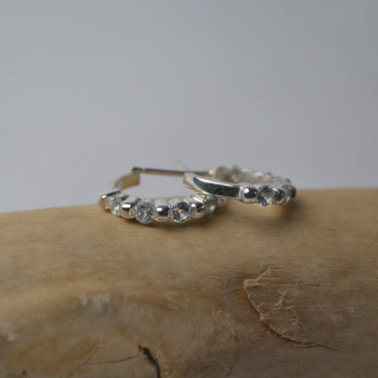 Silver hoop earrings with small stones on a wooden surface
