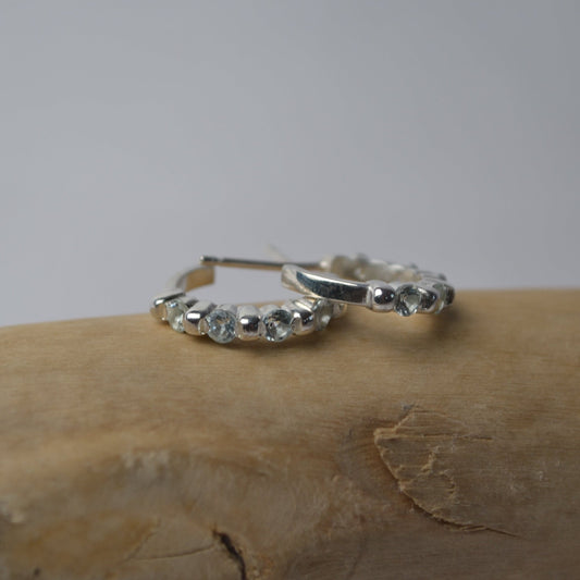 Silver hoop earrings with small stones on a wooden surface