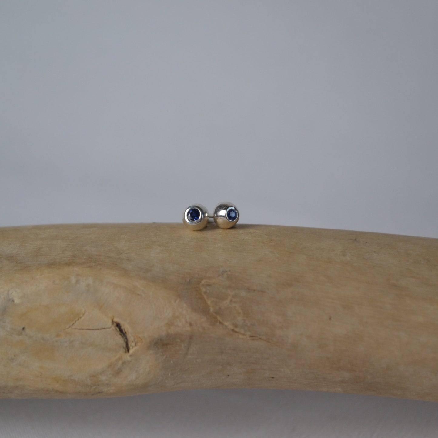 Silver earrings on a piece of driftwood against a plain background