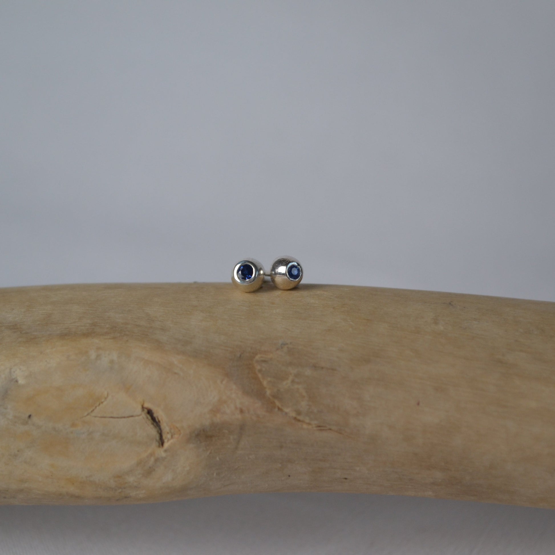 Silver earrings on a piece of driftwood against a plain background