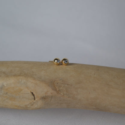 Gold earrings on a wooden branch against a gray background