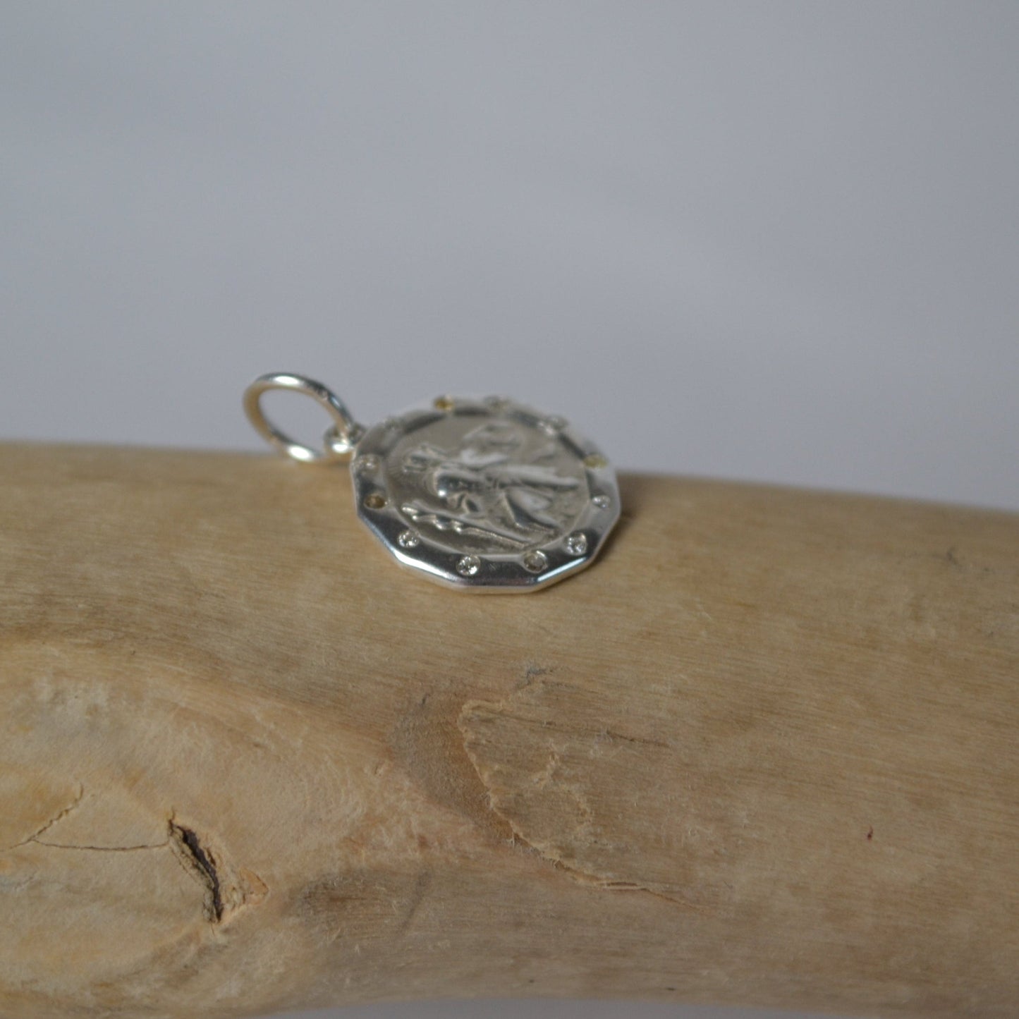 Silver pendant on a wooden stick against a plain background