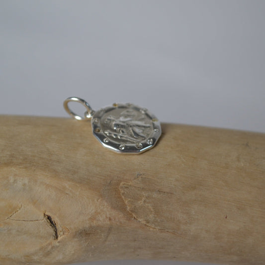 Silver pendant on a wooden stick against a plain background