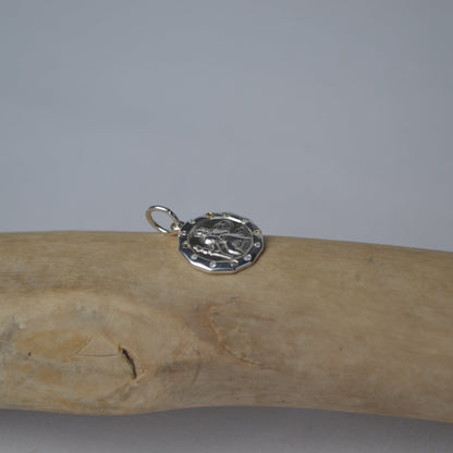 Silver pendant on a wooden stick against a gray background