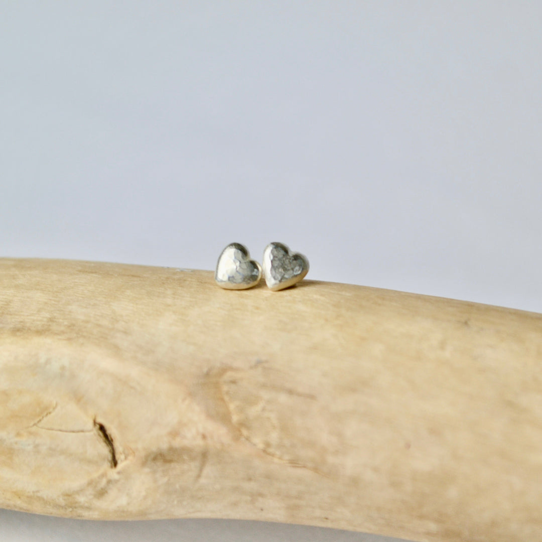 Heart-shaped earrings on a piece of driftwood with a light gray background