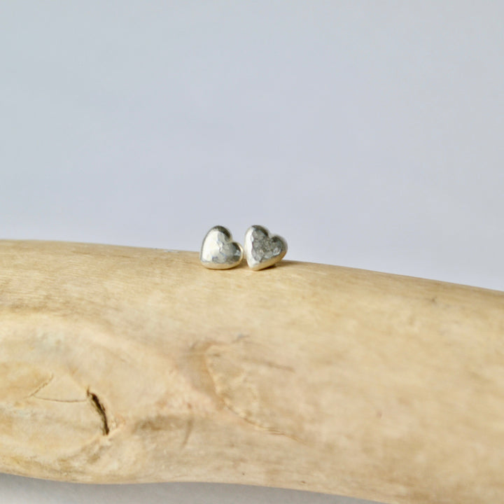 Heart-shaped earrings on a piece of driftwood with a light gray background