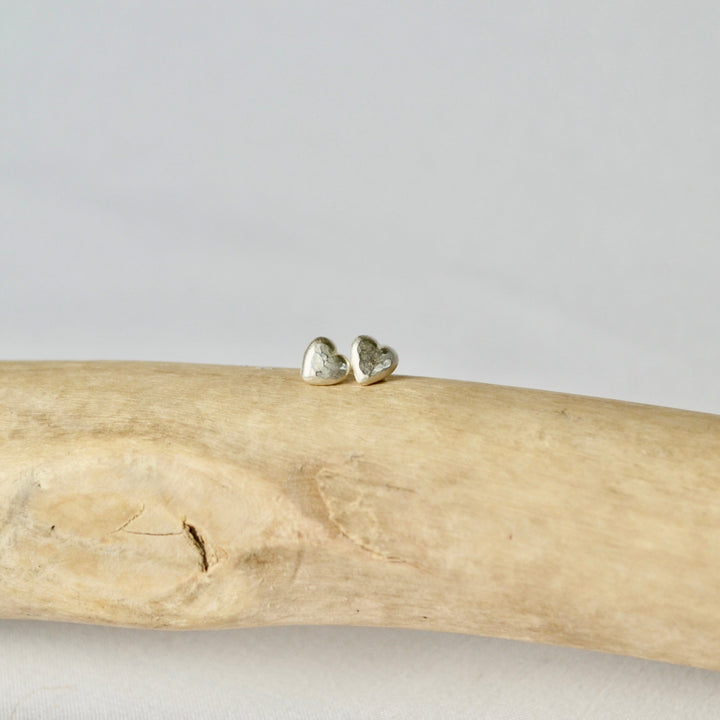 Heart-shaped earrings on a piece of driftwood with a plain background
