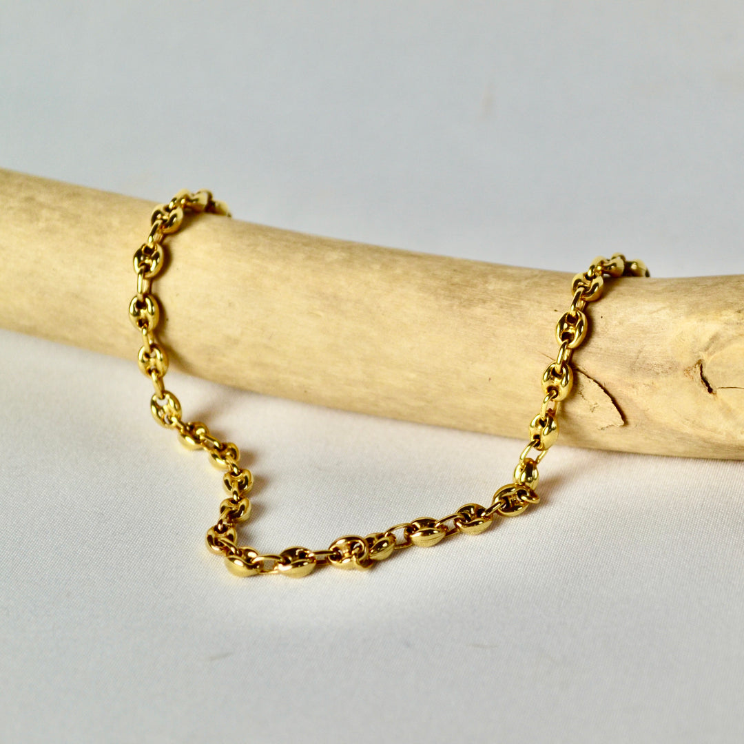 Gold chain bracelet on a wooden stick with a light gray background