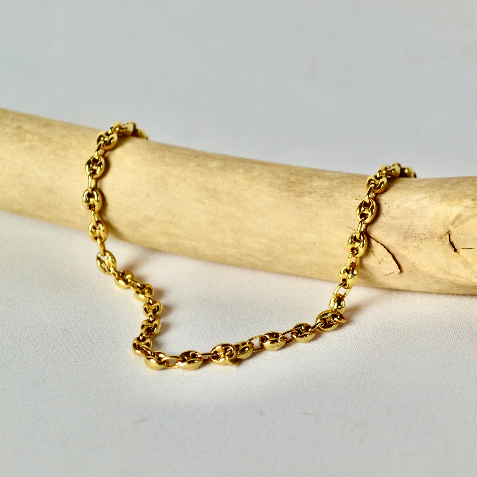 Gold chain bracelet on a wooden stick with a light gray background