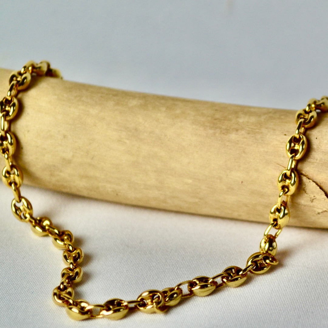 Gold chain necklace on a wooden block with a neutral background