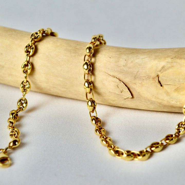 Gold chain necklace on a wooden stick with a white background